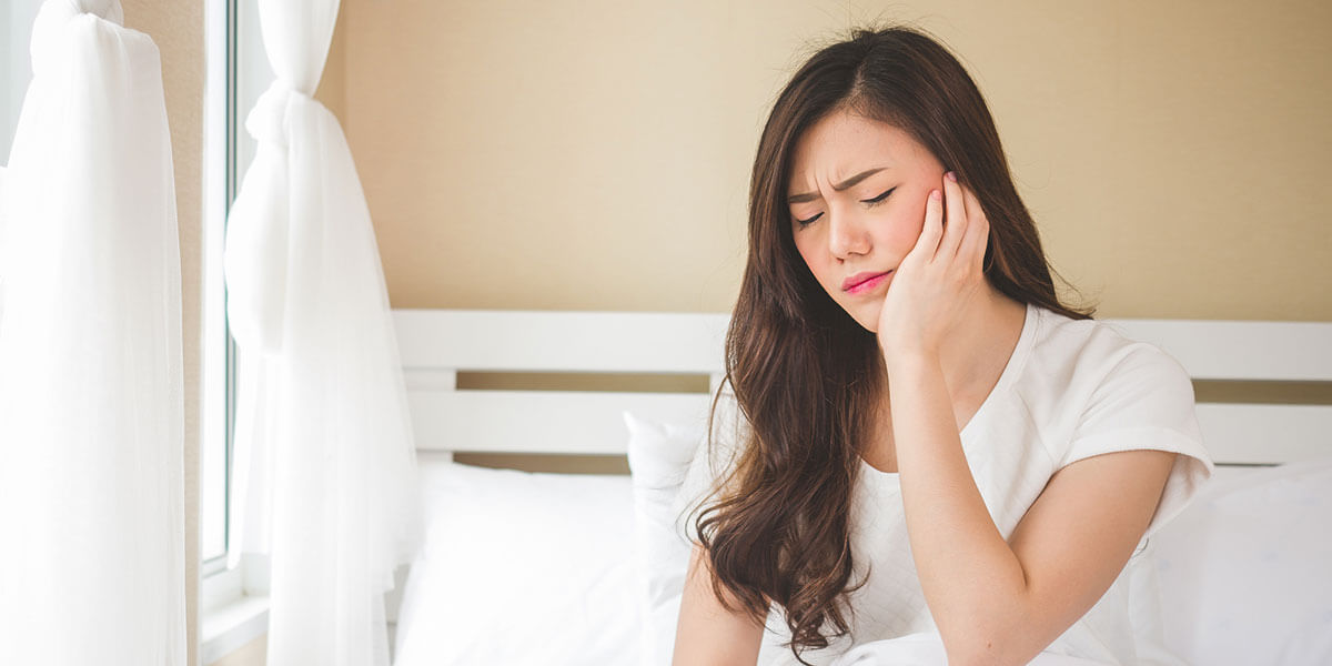 young woman in bed holding jaw in pain