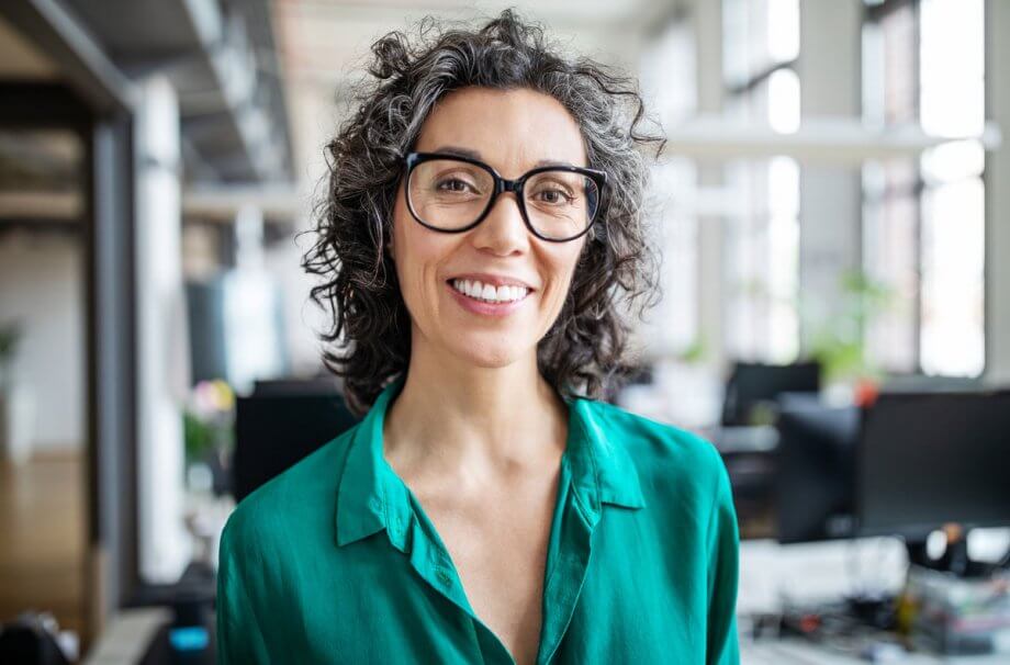 smiling older woman in green blouse and black-rimmed glasses